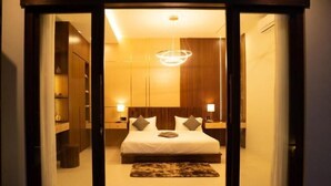 Une chambre d’hôtel avec un lit, des tables de chevet, un lustre et une vue sur l’extérieur, visible à travers une porte vitrée.