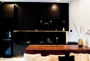 A modern kitchen with dark cabinetry, a wooden dining table, and a vase with dried plants. - VIP Villas and Wellness Resort in Kuta Lombok (Pujut)