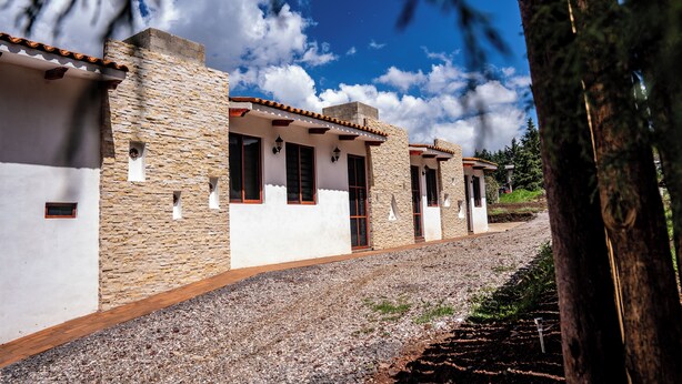 A row of stone and white buildings with a gravel path, surrounded by trees. - Hotel Boutique Cielito Lindo (Jilotepec)
