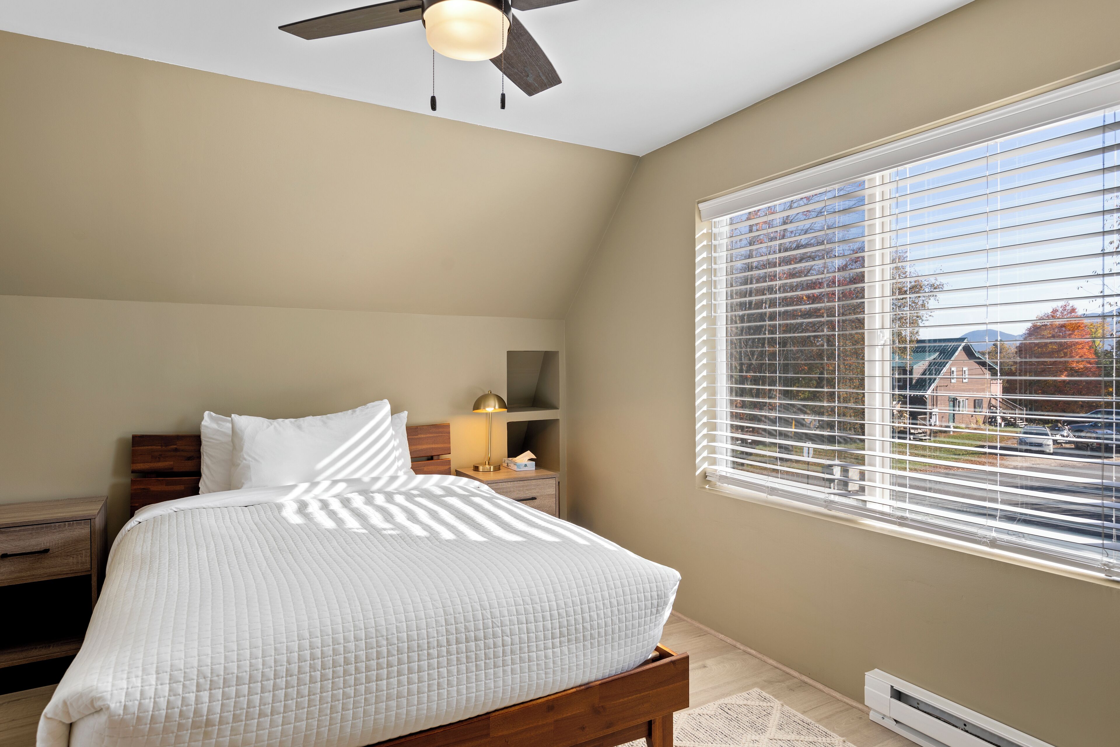 A bedroom with a bed, bedside table, lamp, and a window with blinds.