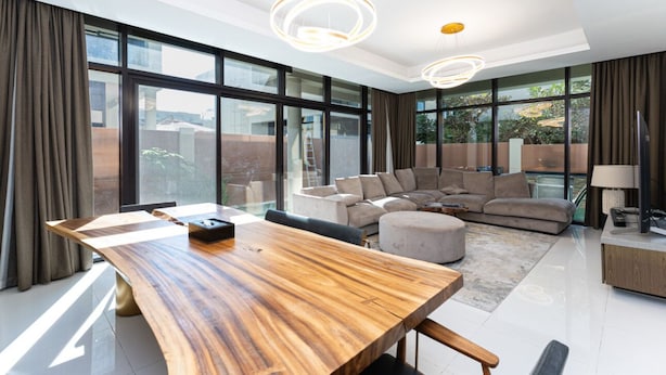 Un salon spacieux avec une grande table en bois, un canapé d’angle et un téléviseur.