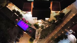 An aerial view of a hotel courtyard with a swimming pool, outdoor seating, and a well-lit walkway.