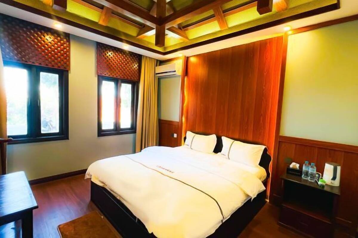 Une chambre d’hôtel avec un grand lit, une tête de lit en bois et une petite table de chevet avec une lampe.