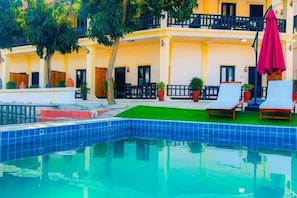 A swimming pool with lounge chairs and umbrellas, surrounded by a building with balconies and potted plants. - YiHao Resort Hotel (Luang Prabang)