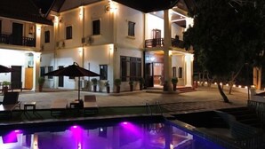 A two-story building with a pool area, outdoor seating, and a well-lit entrance.