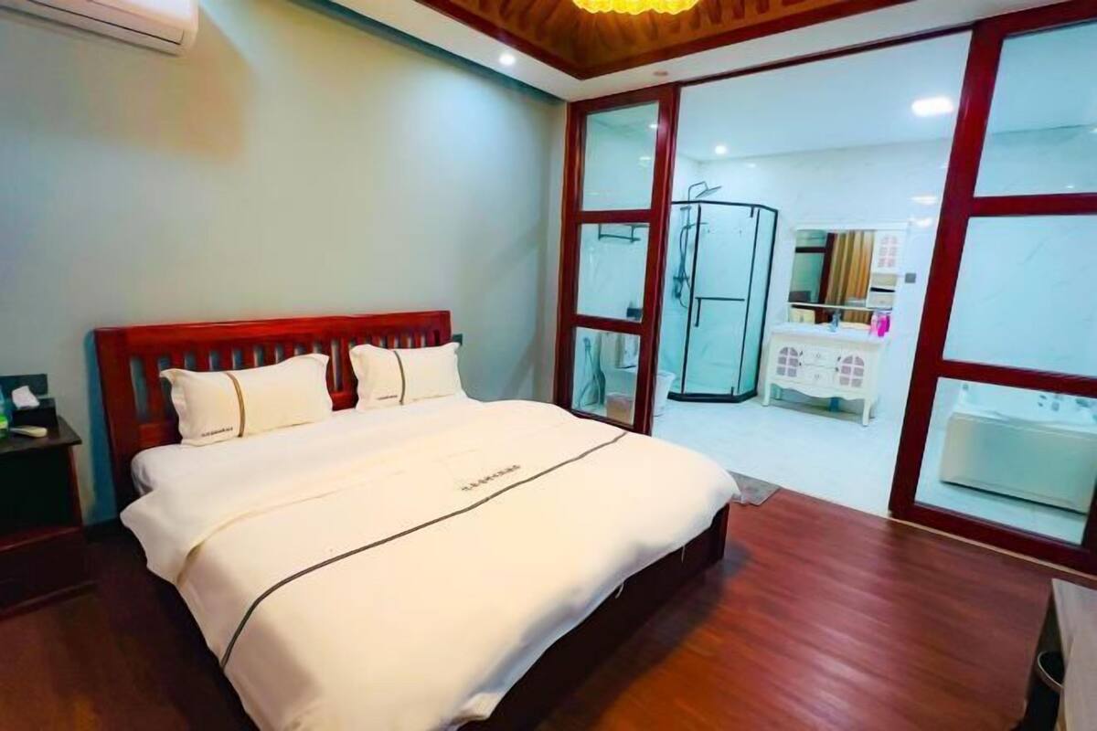 Une chambre d’hôtel avec un lit en bois, une grande fenêtre et une salle de bain visible à travers la porte en verre.