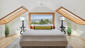A bedroom with a large bed, two bedside lamps, a window with a view, and a skylight. - Luxe Oceanview Game Room Retreat in Ideal Location (Daly City)