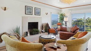 A spacious living room with a fireplace, comfortable seating, and a large window offering a scenic view. - Luxe Oceanview Game Room Retreat in Ideal Location (Daly City)