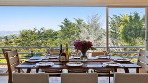 A dining table set for six with wine bottles, glasses, and a vase of flowers, overlooking a scenic landscape. - Luxe Oceanview Game Room Retreat in Ideal Location (Daly City)