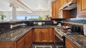 A kitchen with granite countertops, wooden cabinets, a stove, and a view of the outdoors. - Luxe Oceanview Game Room Retreat in Ideal Location (Daly City)