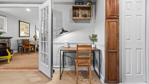 A room with a desk, chair, and a wooden cabinet. There is a white door and a shelf with plants.