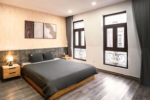 Una camera da letto con un letto, comodini, un'opera d'arte appesa al muro e ampie finestre con persiane.