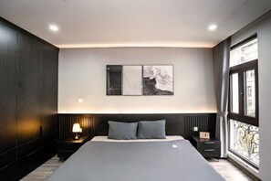 A modern bedroom with a large bed, a nightstand with a lamp, a wall-mounted artwork, and a window with curtains. - Merci Hoang Huy Riverside Hai Phong (Haiphong)