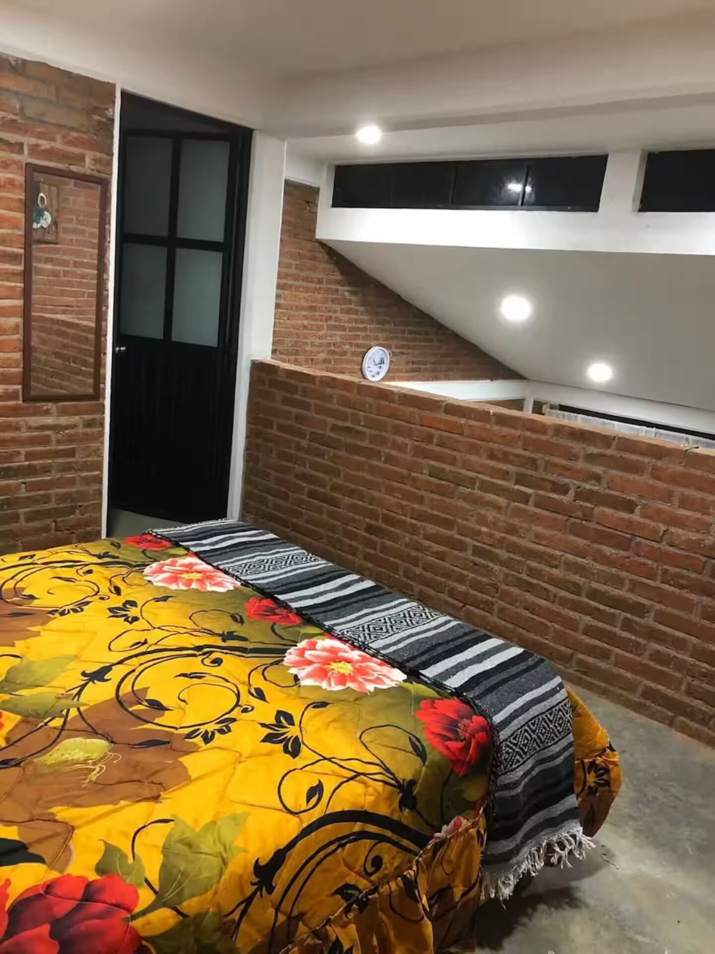 Una stanza con un letto ricoperto da una coperta a motivi floreali, una porta nera e un muro in mattoni.