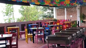 Un espacio de comedor al aire libre con decoraciones de papel de colores y una variedad de sillas y mesas de colores vivos.
