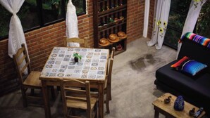 Una habitación acogedora con una mesa con azulejos, sillas de madera, un sofá con cojines coloridos y una pequeña mesa de madera con objetos decorativos.