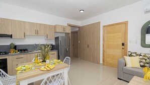 A modern kitchen with wooden cabinets, a stainless steel refrigerator, and a dining area with a table set for two.