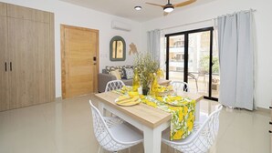 A modern living room with a dining table, white chairs, a ceiling fan, and a view of the outside balcony.