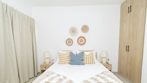 A bedroom with a bed, two nightstands, a wooden wardrobe, and a window with curtains.