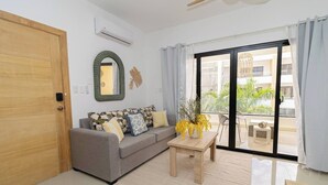A modern living room with a grey sofa, a wooden coffee table, and a large sliding glass door leading to an outdoor balcony.