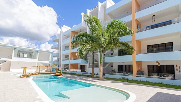 A modern apartment building with a swimming pool, palm trees, and a staircase leading to the upper floors.