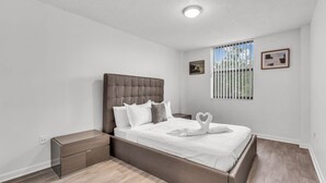 A bedroom with a bed, nightstands, a window with blinds, and a ceiling light. - North Miami 2BR | Pool + Free Parking (North Miami)