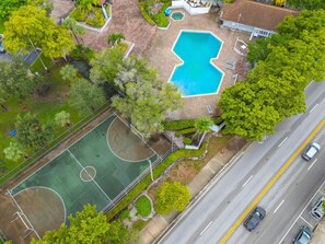 Vue aérienne d’une propriété dotée d’une piscine, d’un terrain de basketball et d’une route adjacente.