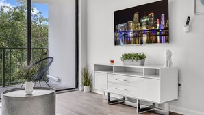 A modern living room with a cityscape painting, a white console table, a black chair, and a small plant. - North Miami 2BR | Pool + Free Parking (North Miami)