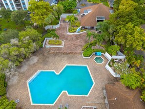 Une vue aérienne d’une piscine à la forme originale, entourée de verdure et bordée d’un bâtiment doté d’un toit en pente.