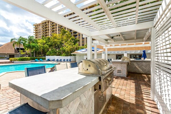 Un espace extérieur avec piscine, barbecue, chaises longues et vue sur un immeuble à plusieurs étages.