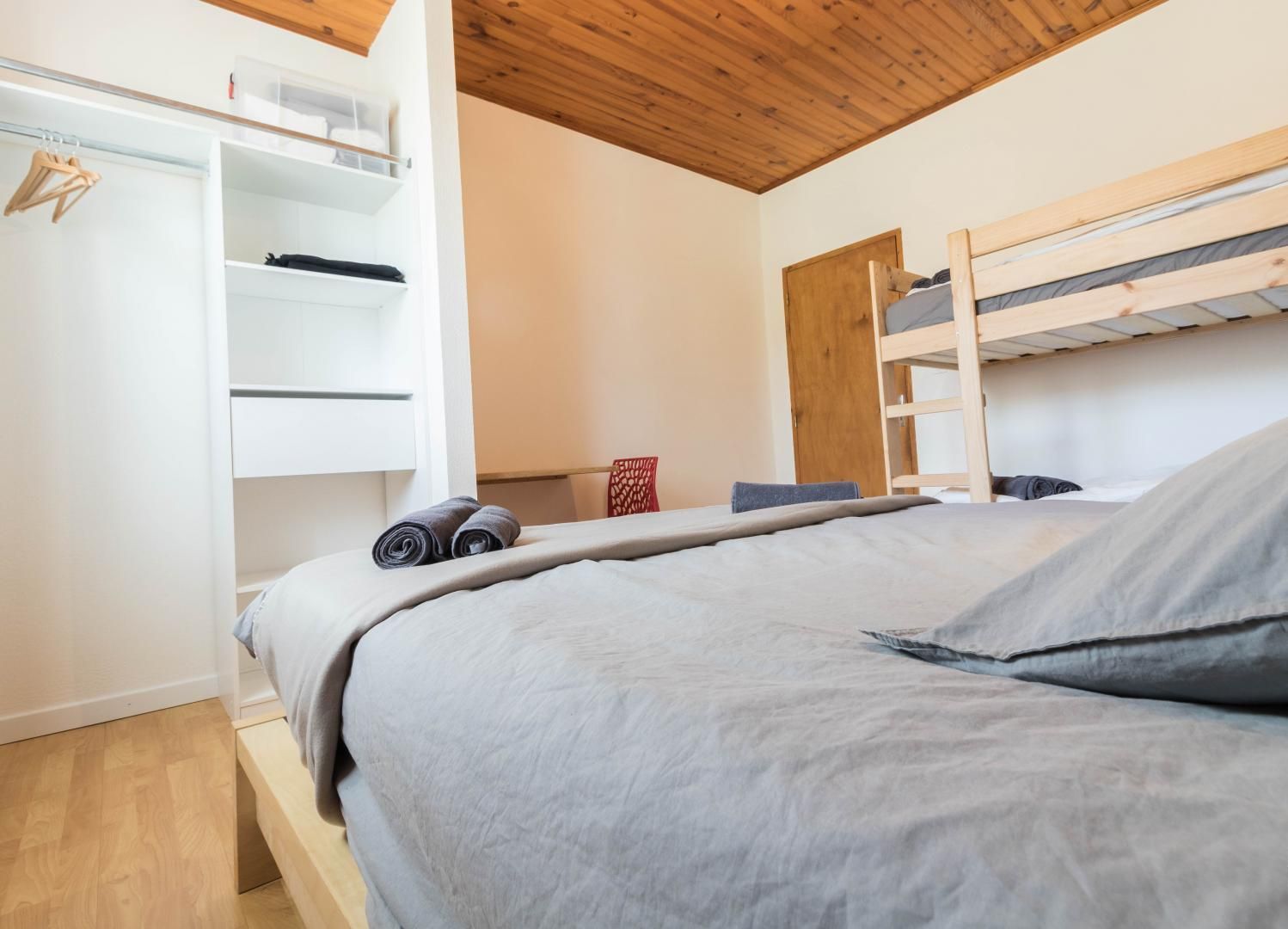Een slaapkamer met een stapelbed, een garderobe met open planken en een houten plafond.