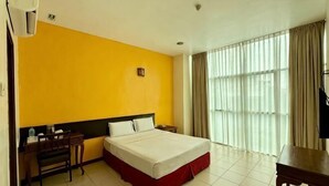 A hotel room with a bed, a desk, a chair, a TV, and a window with curtains.