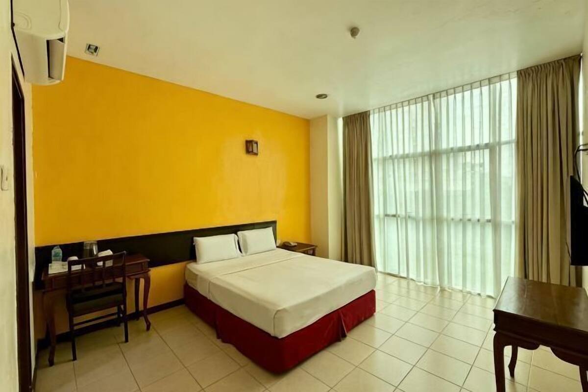 Een hotelkamer met een bed, een bureau, een stoel, een televisie en een raam met gordijnen.