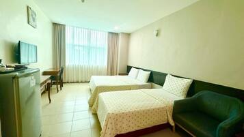 Quarto de hotel com duas camas, uma escrivaninha com cadeira, televisão e frigorífico.
