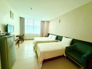 A hotel room with two beds, a desk with a chair, a television, and a refrigerator. - Grand Far East Hotel (Masai)