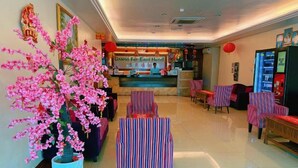 Hall d'hotel con reception, area salotto e grande composizione floreale rosa artificiale.