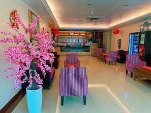 A hotel lobby with a reception desk, seating area, and a large artificial pink flower arrangement. - Grand Far East Hotel (Masai)