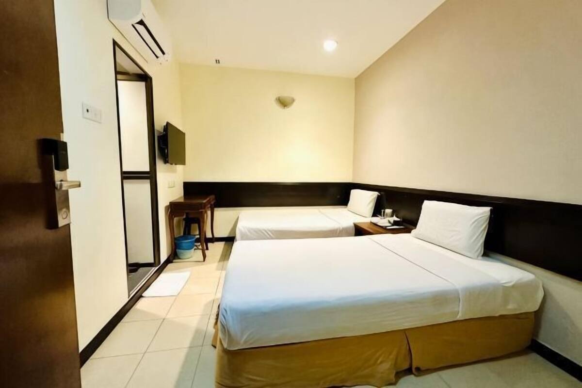 Een hotelkamer met twee bedden, een bureau, een stoel, een televisie en een deur.