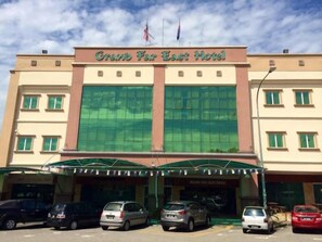 A hotel with a large glass facade, a covered entrance, and multiple parking spaces. - Grand Far East Hotel (Masai)