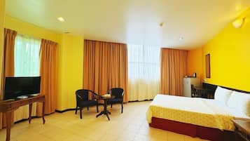 Quarto de hotel com cama, escrivaninha, televisão e duas cadeiras.