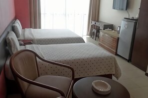 Een hotelkamer met twee bedden, een stoel, een klein tafeltje, een televisie en een dressoir.