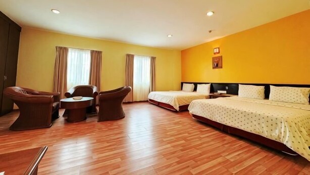 A hotel room with a wooden floor, two beds, a desk, and a chair.