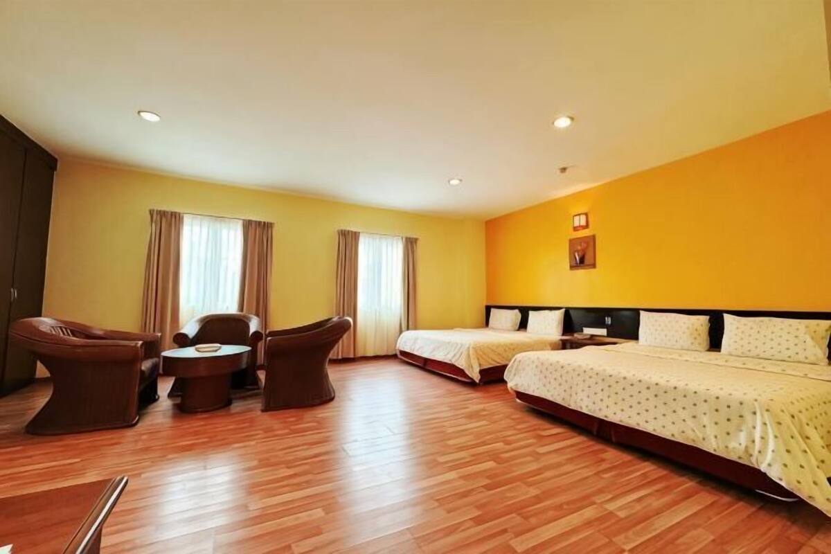 Een hotelkamer met een houten vloer, twee bedden, een bureau en een stoel.