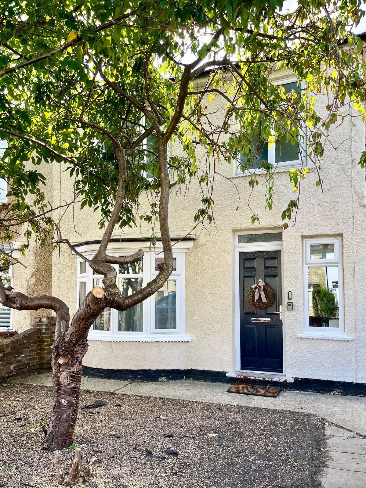A building with a traditional facade, a black door with a wreath, and a tree in the foreground.