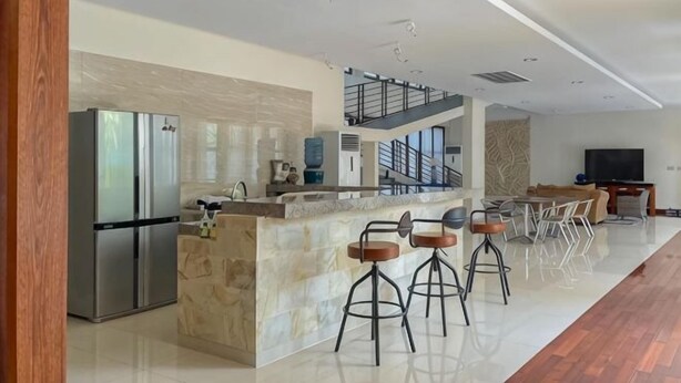 A modern kitchen with a marble island, stainless steel appliances, and a dining area with bar stools. - Merbau Luxurious Villa Senggigi by The Lavana (Batu Layar)