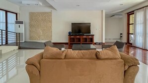 A living room with a sofa, a television on a stand, a patterned wall, and a large window. - Merbau Luxurious Villa Senggigi by The Lavana (Batu Layar)