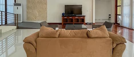 A living room with a sofa, a television on a wooden stand, and a patterned wall.
