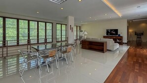 A spacious living area with a glass dining table, sofas, and a TV. - Merbau Luxurious Villa Senggigi by The Lavana (Batu Layar)