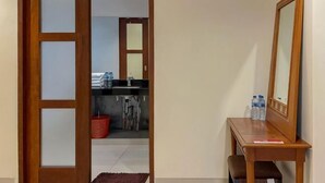A room with a wooden door, a mirror, a desk, and a view into a kitchen area. - Merbau Luxurious Villa Senggigi by The Lavana (Batu Layar)