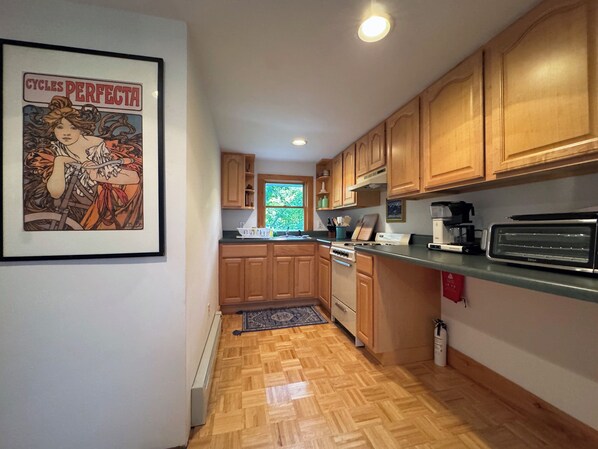 Una cocina con armarios de madera, una estufa, un tostador y un cuadro en la pared.